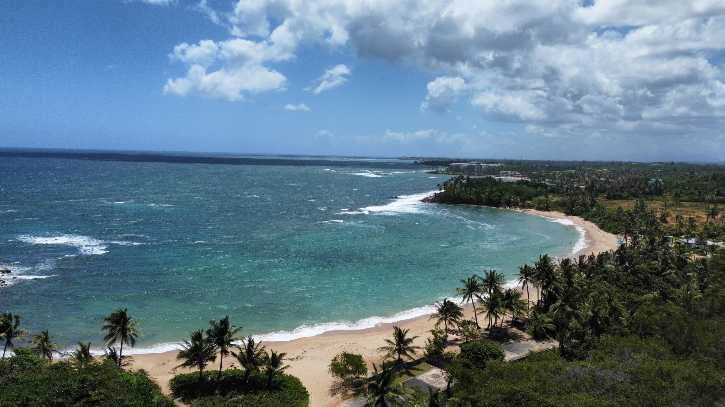 Aerial view of the beach bordering Lakeside Villas, with turquoise water and palm-lined shoreline