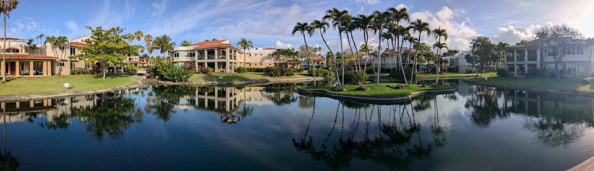 Panoramic view across the community lake, with palms and villas reflected on the water
