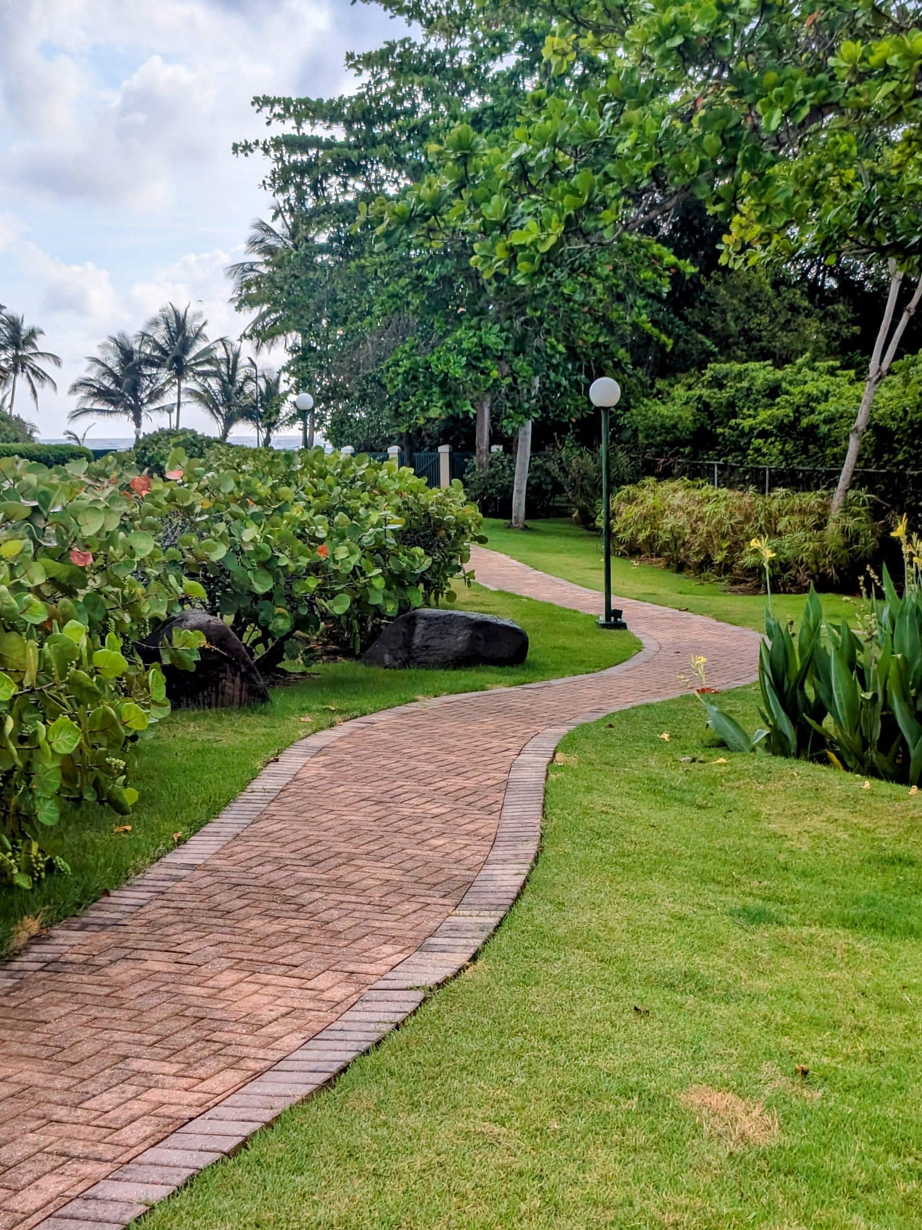 Curved brick pathway winding through tropical landscaping toward the beach