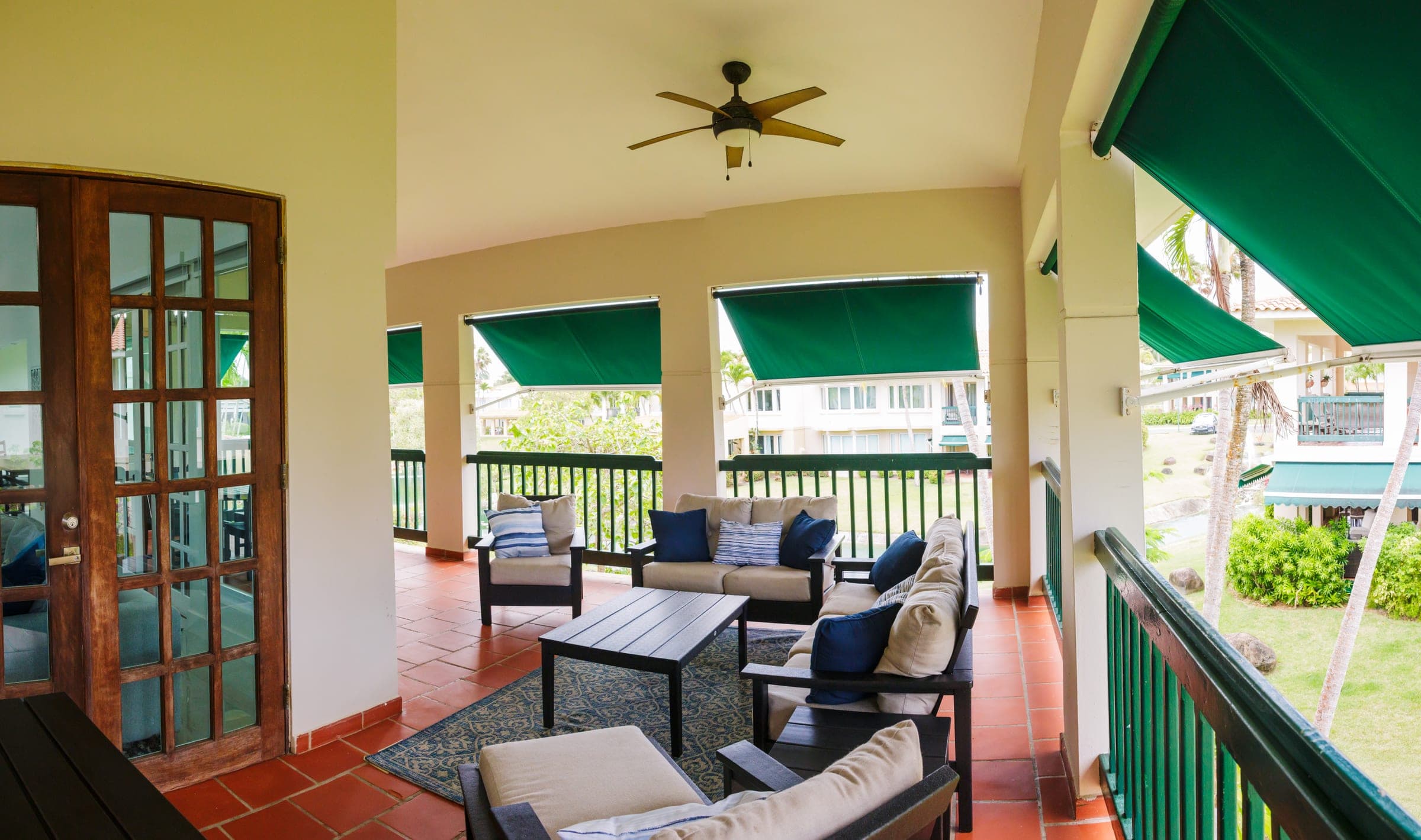 Covered porch with lounge seating, ceiling fan, and retractable awnings overlooking the community grounds
